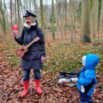 Outdoor Musikschule Göttingen: Franziska Näther steht im Regen beim Musizieren im Wald, ein Kind schaut gebannt und begeistert zu
