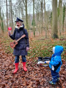 Outdoor Musikschule Göttingen: Franziska Näther steht im Regen beim Musizieren im Wald, ein Kind schaut gebannt und begeistert zu