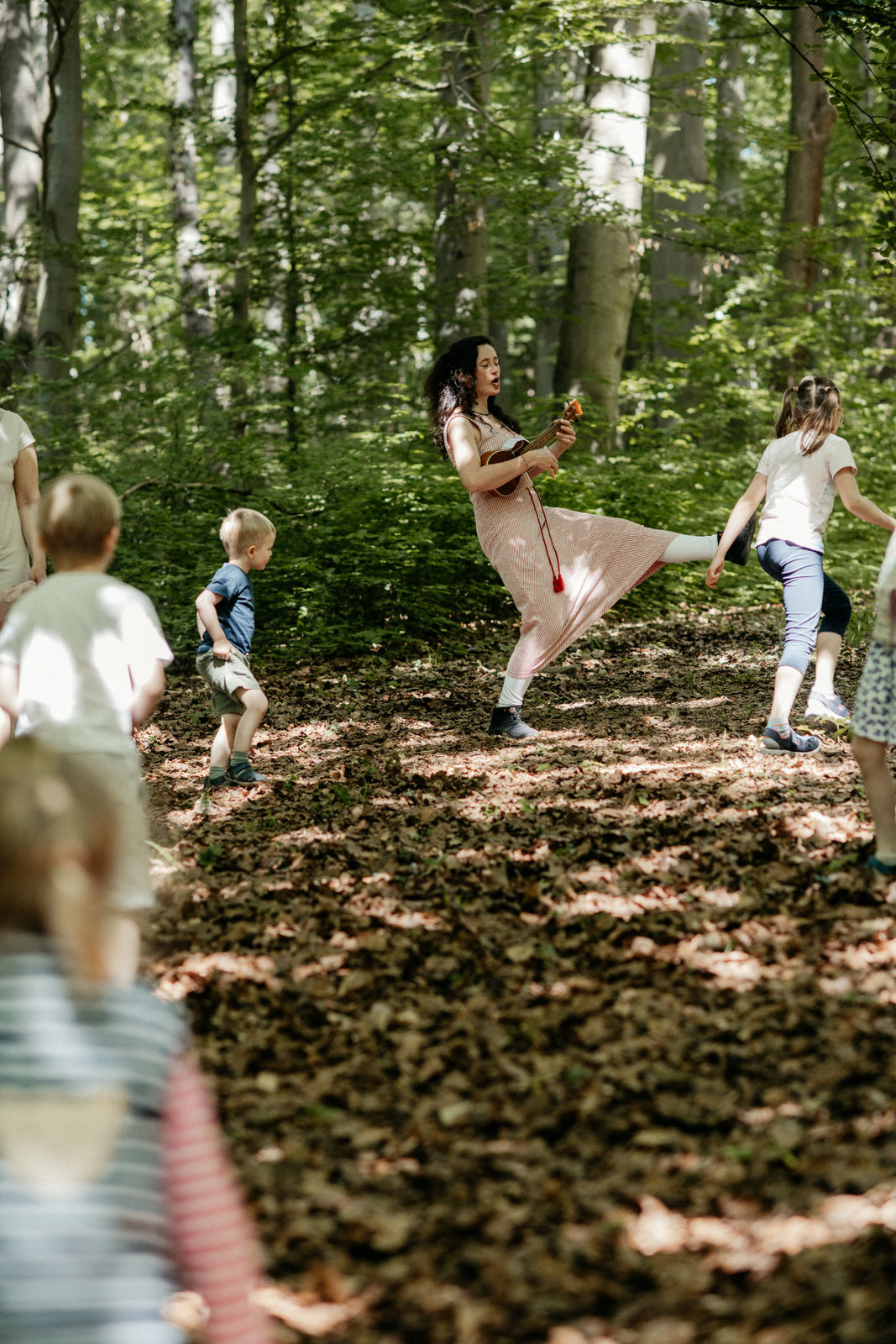 Musizierende Kinder rennen fröhlich im Wald, Franziska Näther singt freie Lieder und spielt Ukulele dazu